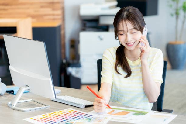 電話をしながら色見本に書き込む事務担当(イメージ)